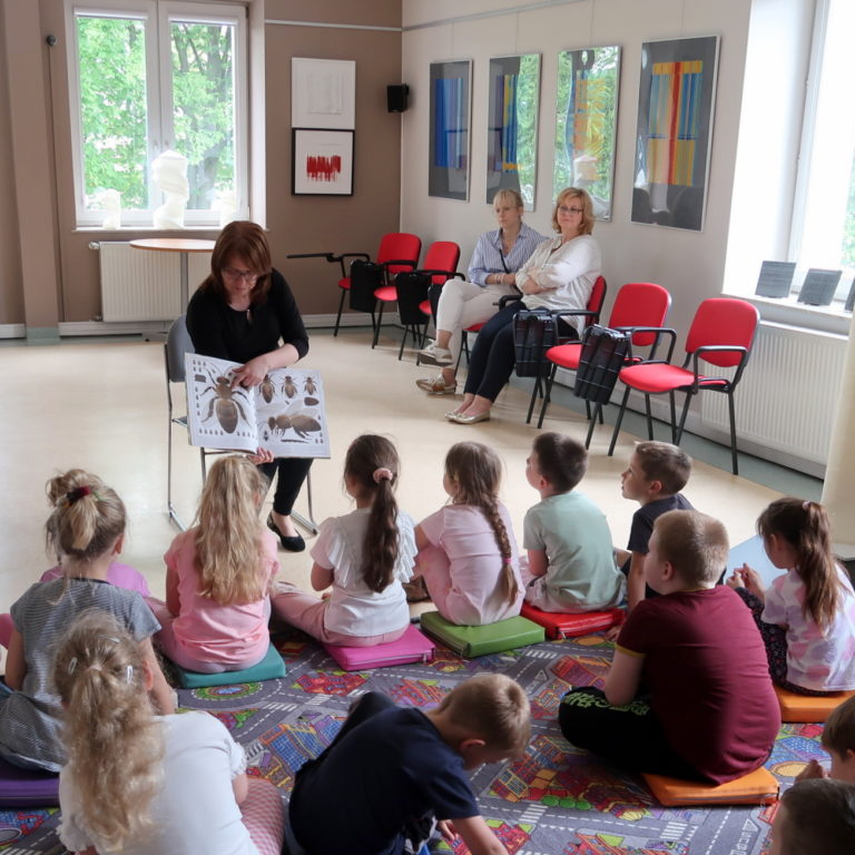 Prowadząca zajęcia bibliotekarka pokazuje dzieciom książkę z obrazkami pszczół